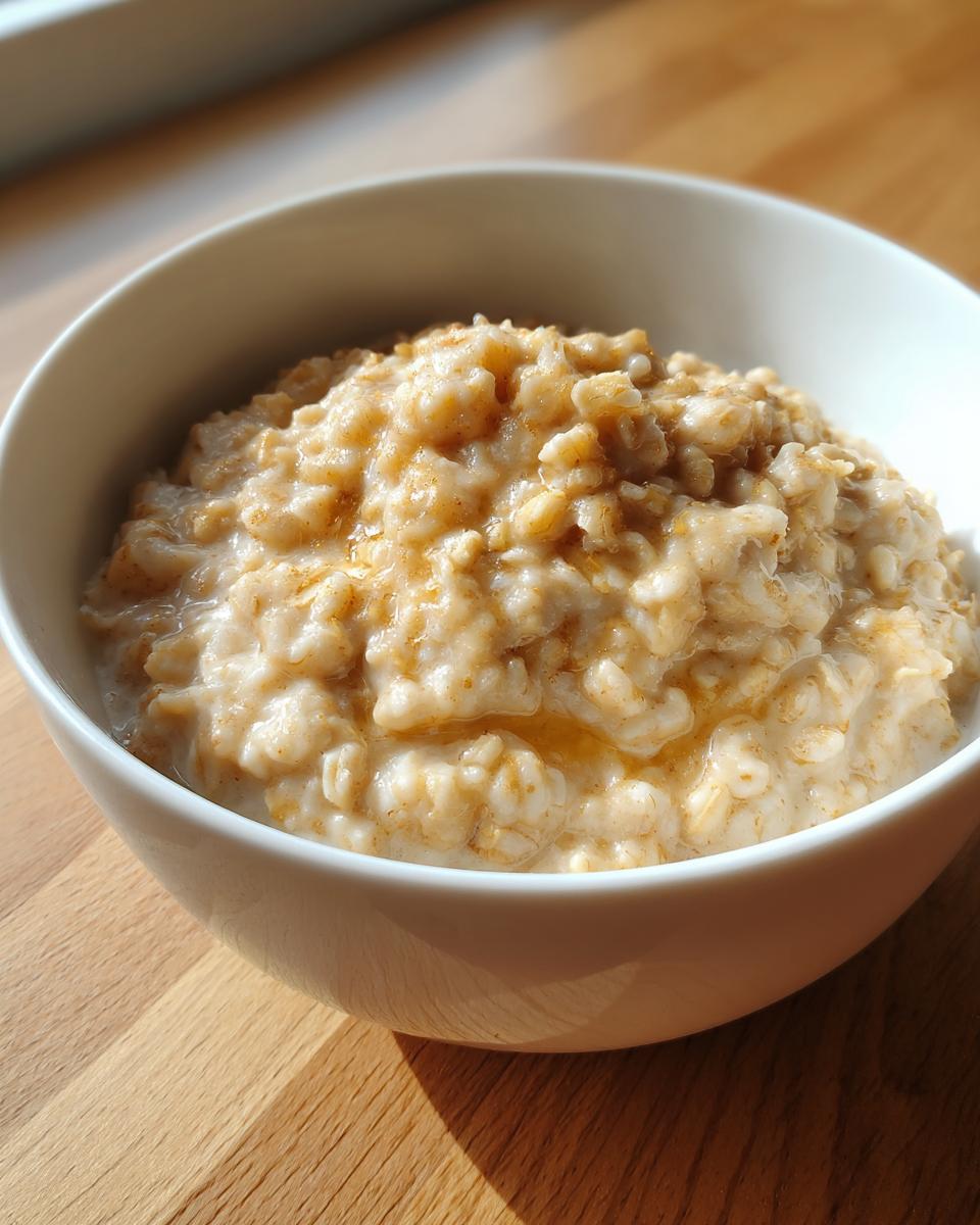 A close-up of creamy banana oatmeal topped with a drizzle of sweetener in a white bowl.