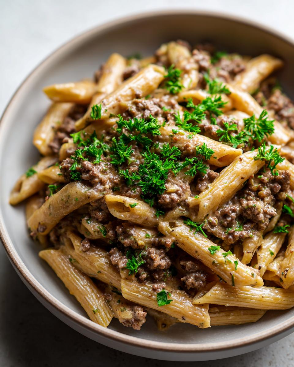 Close-up of creamy beef pasta featuring penne noodles coated in a rich sauce and topped with ground beef and fresh parsley.