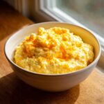 A close-up of a bowl filled with creamy, yellow cheese grits topped with melted orange cheddar cheese.