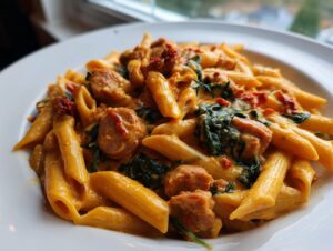 Close-up of creamy chicken sausage pasta featuring penne noodles, sliced sausage, spinach, and sun-dried tomatoes.