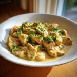 Close-up of tender pieces of coconut chicken coated in a rich, creamy sauce and garnished with fresh parsley.