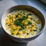 Close-up of a bowl of rich, creamy corn chowder loaded with yellow corn kernels, potato chunks, and fresh parsley.