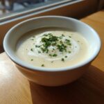 A creamy bowl of amazing garlic soup topped with a swirl of cream and fresh chopped parsley.