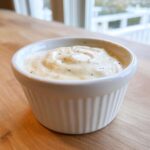 A close-up of thick, creamy horseradish sauce speckled with pepper in a small white fluted ramekin.