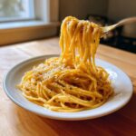 A fork lifts a generous portion of creamy lemon pasta coated in sauce, topped with grated cheese and black pepper.