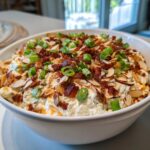 A creamy, cheesy Neiman Marcus dip topped generously with bacon bits, sliced almonds, and chopped green onions.