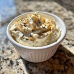 A close-up of creamy homemade onion dip topped with caramelized onions and herbs in a white bowl.