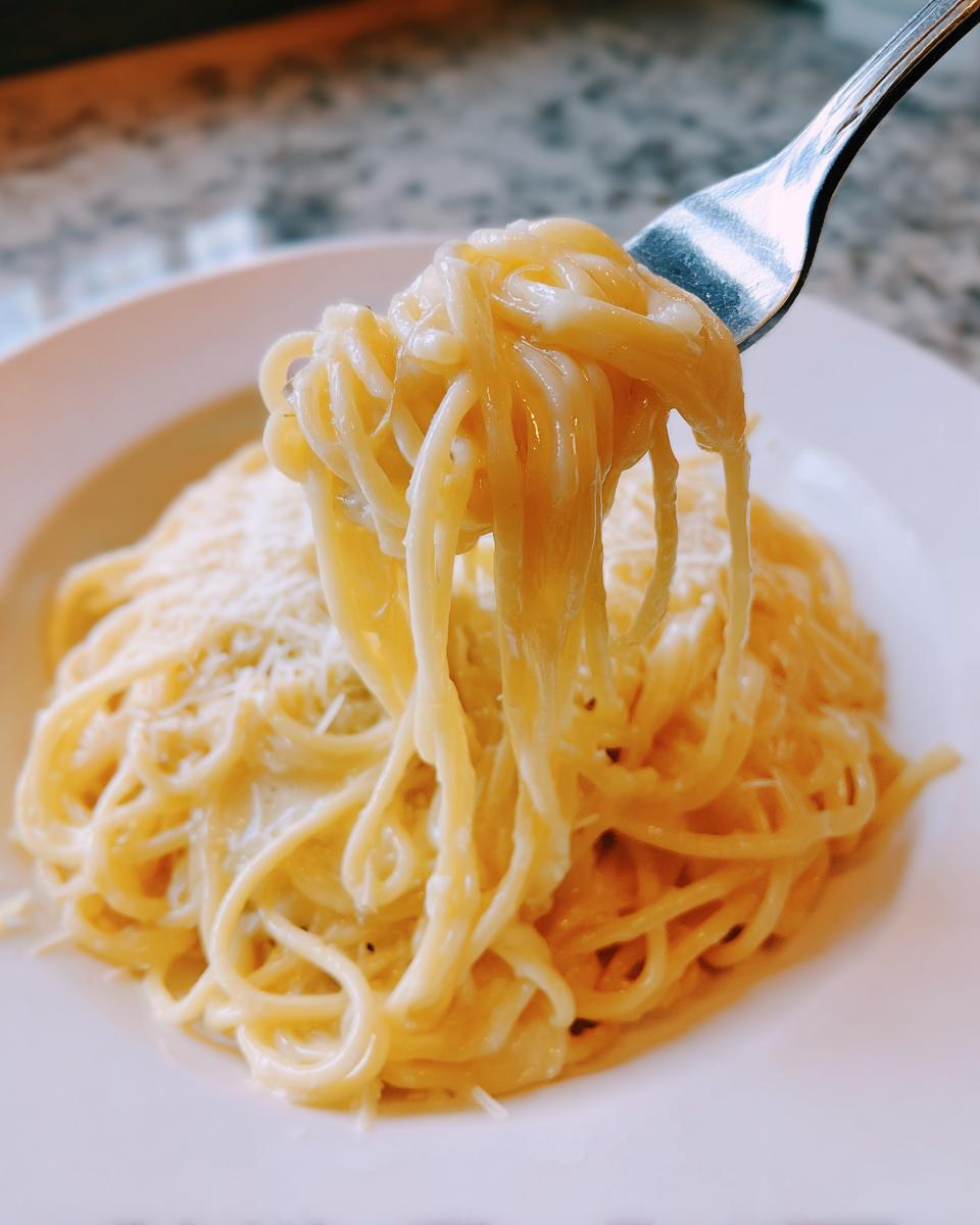 Close-up of a fork lifting creamy strands of spaghetti from a plate of amazing parmesan pasta.