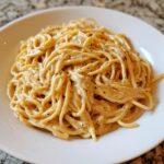 Close-up of a generous serving of creamy parmesan pasta coated in a rich sauce and sprinkled with black pepper.