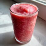 Close-up of a frosty, bright red watermelon smoothie in a tall glass, glistening with condensation.