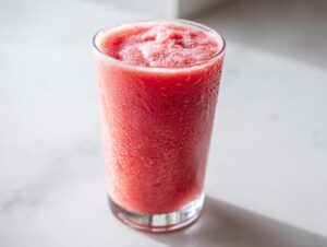 A tall glass filled with a vibrant, icy watermelon smoothie, showing condensation droplets on the outside.