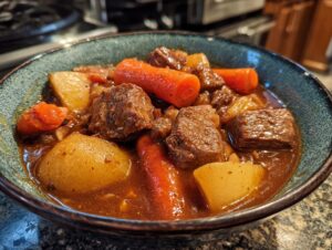 Close-up of a rustic bowl filled with rich crockpot beef stew featuring tender beef chunks, large carrots, and potatoes.
