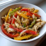 Close-up of shredded chicken mixed with colorful bell peppers and onions, seasoned for crockpot chicken fajitas.