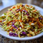 A vibrant mound of crunchy cabbage salad featuring shredded green cabbage, purple cabbage, and bright orange carrots tossed in a light dressing.