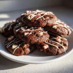 A stack of fudgy double chocolate peppermint cookies drizzled with white icing and topped with crushed candy canes.