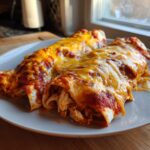 Two delicious easy chicken enchiladas covered in melted red sauce and cheddar cheese on a white plate.