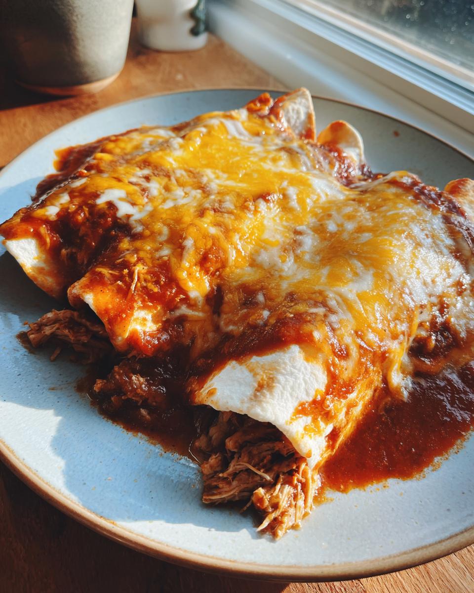 Two rolled tortillas filled with shredded chicken, smothered in red sauce and melted cheddar cheese, ready to eat easy chicken enchiladas.