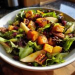 Close-up of a vibrant fall harvest salad featuring roasted squash cubes, apple slices, pecans, and dried cranberries over mixed greens.
