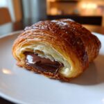 Close-up of a flaky, golden brown chocolate croissant cut open to show gooey melted chocolate filling.