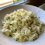 A close-up of fluffy cilantro lime rice garnished with chopped cilantro and lime zest in a white bowl.