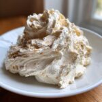 A mound of fluffy, whipped honey butter recipe mixture dusted lightly with cinnamon on a white plate.