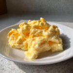 A serving of incredibly fluffy, creamy scrambled eggs piled high on a white plate.