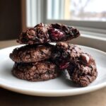 A stack of three fudgy chocolate cherry cookies, one broken open to show the gooey cherry filling and melted chocolate chips.