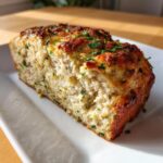 Close-up of a moist slice of Garlic Parmesan meatloaf, topped with browned cheese and fresh parsley.