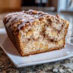 A close-up, cross-section view of a freshly baked apple fritter bread loaf drizzled with white icing.