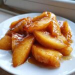 Close-up of warm, glistening apple pie filling slices coated in a rich, cinnamon-brown glaze on a white plate.
