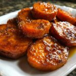 Close-up of thick-cut, glossy candied sweet potatoes slices piled on a white dish.