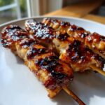 Three glossy, caramelized chicken skewers resting on a white plate, showcasing a rich glaze.