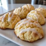Several freshly baked ricotta cookies topped with a sweet white glaze, arranged on a white platter.