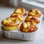 Six golden brown baked egg bites cooling in a white ceramic muffin tray, perfect for meal prep.