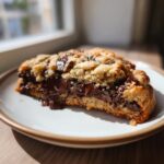 A cross-section of a thick levain bakery chocolate chip cookie showing melted, gooey chocolate chips.