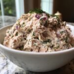 Close-up of a generous bowl of healthy tuna salad mixed with red onion and topped with fresh dill.