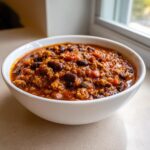 Close-up of a white bowl filled with rich, thick high protein chili featuring ground meat and dark kidney beans.