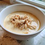 A white bowl filled with creamy homemade cream of chicken soup topped generously with shredded chicken.