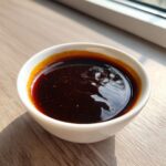 Close-up of thick, glossy homemade teriyaki sauce in a small white bowl on a wooden surface.