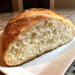 Close-up of a freshly baked italian bread loaf cut in half, showing an airy, open crumb and golden crust.