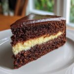 A close-up of a slice of rich, dark chocolate Italian love cake featuring a creamy yellow filling layer.