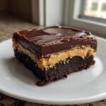 A single, thick square of layered buckeye brownies featuring a dark chocolate base, peanut butter filling, and chocolate ganache topping.