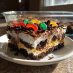 A decadent slice of layered dirt cake showing chocolate, cream, and pudding layers, topped with crushed cookies and gummy candies.