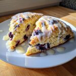 Two triangular slices of lemon blueberry scones topped with a thick white glaze, served on a white plate.