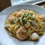 Close-up of creamy fettuccine seafood pasta featuring large shrimp and scallops, topped with parsley.
