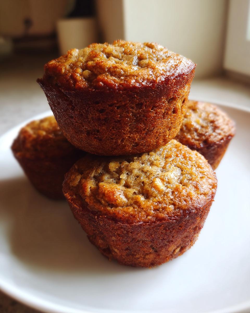 A close-up stack of three golden brown, moist oatmeal muffins sitting on a white plate.