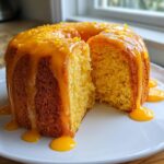 A slice cut from a moist orange juice cake topped with a thick orange glaze and zest.