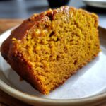 Close-up of a moist, richly colored slice of pumpkin bread on a small plate.