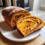 A loaf of vibrant orange pumpkin sourdough bread, partially sliced, showing a moist crumb and cinnamon swirl.