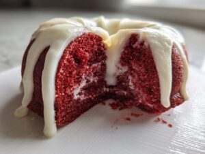 Close-up of a slice taken out of a moist red velvet bundt cake topped with dripping white cream cheese glaze.